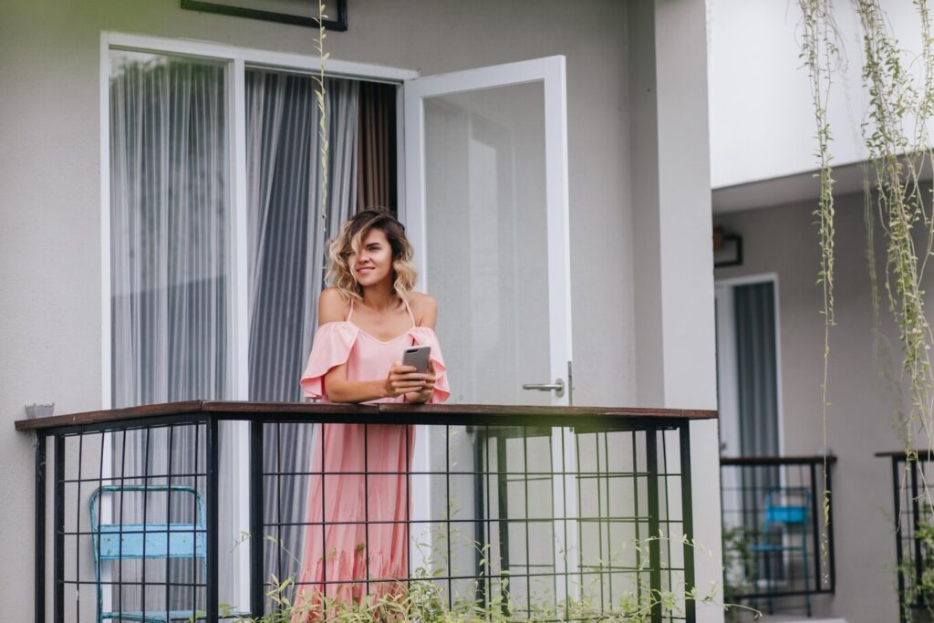 glamorous-curly-lady-standing-balcony-with-smartphone-charming-caucasian-girl-looking-city-from-terrace_197531-9078